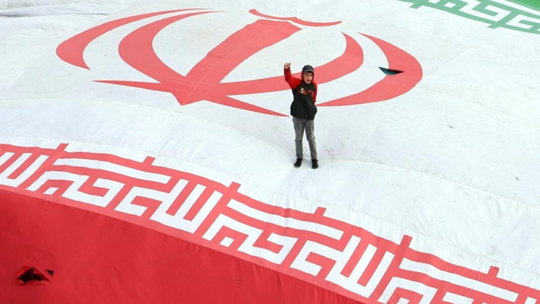 A boy raises his fist while standing on a giant Iranian flag during the funeral of Alireza Tangsiri, commander of the Iranian Revolutionary Guards' navy, alongside others killed in US-Israeli strikes on Iran at Enghelab Square in Tehran on April 1, 2026. 