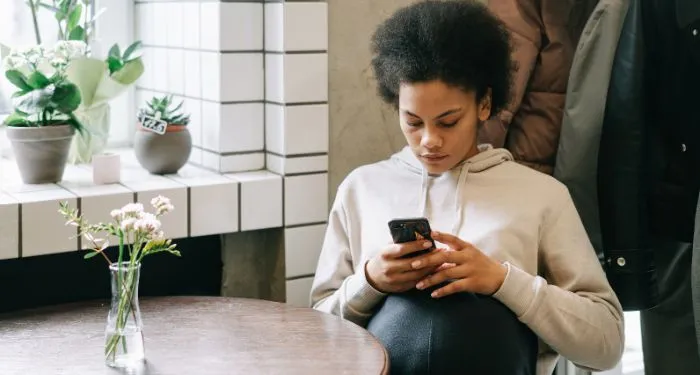 Image of a Black woman reading on her phone at a table
